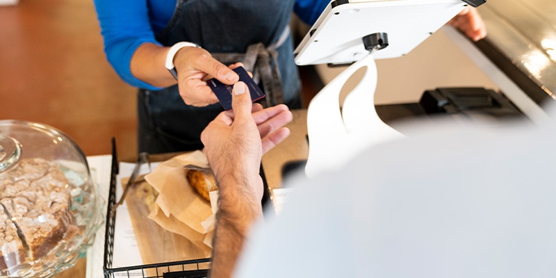 A Honor Bank customer handing over their debit card to a bakery worker.