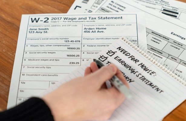 A stack of W2 tax forms and someone taking notes on a notepad.