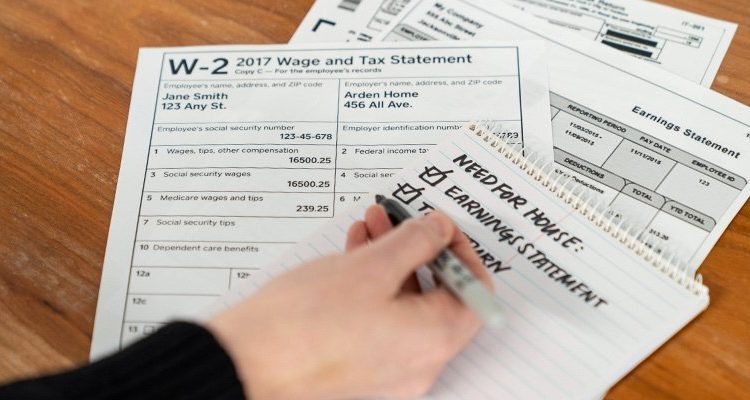 A stack of W2 tax forms and someone taking notes on a notepad.