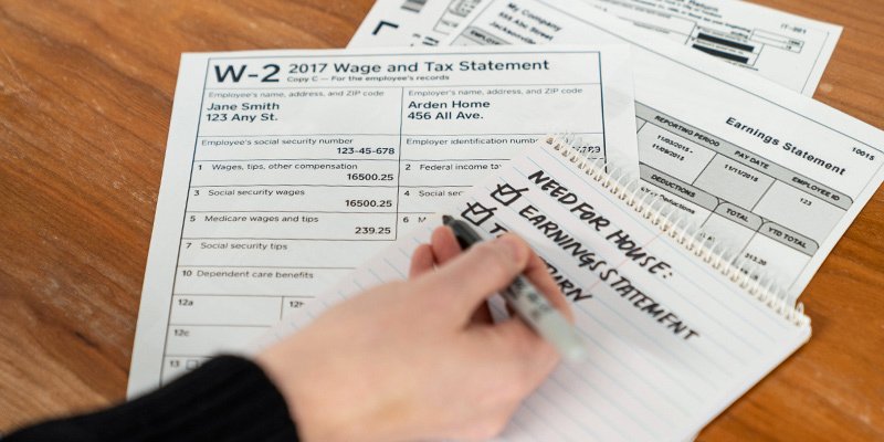 A stack of W2 tax forms and someone taking notes on a notepad.