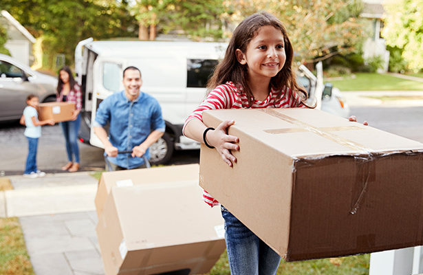 A young family moving into their new house. A young child carrying a box into their new house.