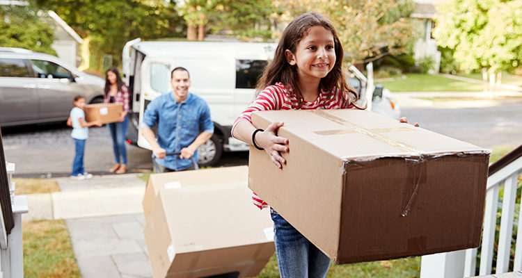 A young family moving into their new house. A young child carrying a box into their new house.