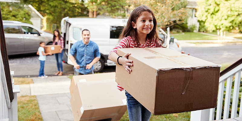 A young family moving into their new house. A young child carrying a box into their new house.