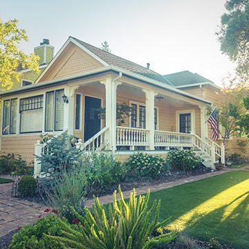 White Picket Fence Home With Veranda And Flag